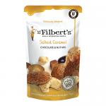 A neat array of fifteen 75g Mr Filberts Salted Caramel Chocolate & Nut Mix packets sits on a textured surface with a muted festive background. Each red and gold wrapper shows the logo, chocolate pieces, nuts and caramel drips, accented by holly sprigs and delicate snowflake patterns. Soft light glow