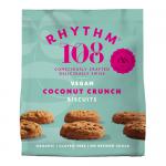 A bright studio image shows a sharing bag of Rhythm 108 Organic tea biscuits sitting beside a tidy stack of round coconut cookies. Golden-brown edges, visible coconut flakes, and scattered crumbs rest on a clean white surface; the bag displays simple earthy graphics. Soft light shows fine texture..