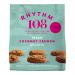 A bright studio image shows a sharing bag of Rhythm 108 Organic tea biscuits sitting beside a tidy stack of round coconut cookies. Golden-brown edges, visible coconut flakes, and scattered crumbs rest on a clean white surface; the bag displays simple earthy graphics. Soft light shows fine texture..