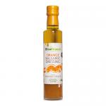 Six slender glass bottles of Olive Branch Orange Balsamic Dressing stand in a neat row, their amber-orange liquid catching light. Each bottle bears a white label with an olive-branch logo and orange illustration, sealed with black caps and arranged against a clean, neutral background. In soft light.