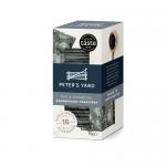 A clean photograph shows a slim box of Peter’s Yard Charcoal & Rye minis beside a handful of dark, thin crispbreads. The box features monochrome charcoal-hued packaging with a minimalist logo; crackers display porous texture, rye flecks, and irregular rustic edges on a light wooden surface. Soft-lit
