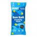 Matte single packs and a tidy column of twelve Brave Roasted Peas Sea Salt 35g sit on a neutral surface. Bold navy logo and crisp white typography contrast with green pea illustrations. A small transparent window reveals golden roasted peas and coarse salt crystals inside. Crisp matte finish borders