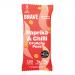Bright red-orange bag of Brave Roasted Peas Paprika & Chilli sits on a wooden surface. Crisp roasted green peas tumble from a torn corner beside scattered paprika powder and red chili slices. Bold typography and spice illustrations decorate the front against a warm gradient backdrop. Soft studio-lit