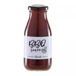 A glossy bottle labeled Hawkshead Relish BBQ Sauce stands beside a tidy arrangement of six assorted Hawkshead Relish dressings and sauces in small bottles. Deep brown sauce shows through glass; colorful labels and a neutral background emphasize textures and branding. Soft lighting casts reflections.