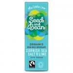 A small, unwrapped milk chocolate mini bar sits beside its kraft paper wrapper; the creamy pale-brown surface is studded with coarse white sea-salt crystals and flecks of vivid green lime zest. Soft shadows and a neutral background highlight the textured chocolate with lime peel shards & soft sheen.