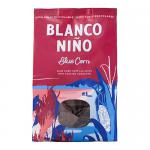 A white, earth-toned bag displays the Blanco Niño logo above a pile of golden triangular ancient-grain tortilla chips. Chips show grain flecks and crisp texture; a few are stacked and scattered beside sprigs of grain. Bold clean typography and rustic accents frame the image. Subtle shadowing overall