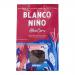 A white, earth-toned bag displays the Blanco Niño logo above a pile of golden triangular ancient-grain tortilla chips. Chips show grain flecks and crisp texture; a few are stacked and scattered beside sprigs of grain. Bold clean typography and rustic accents frame the image. Subtle shadowing overall