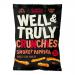 Photo shows ten 30g Well & Truly Crunchy Paprika packets arranged in two rows on a white background. Each packet displays a red-orange color block, a paprika illustration, the Well & Truly logo in white, bold product name in dark type, and a close-up of crunchy snack pieces.