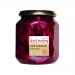 A clear glass jar displays deep purple shredded red cabbage mixed with pale apple slices and specks of mustard seed. A simple cream label wraps the jar with black text stating the name and a small logo. The metal lid reflects studio lights. Dew droplets bead on the glass; a faint shadow sits below..
