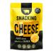 A vibrant retail display shows a stack of glossy snack boxes labeled Serious Pig, featuring a stylized pig logo. The foreground reveals golden, crunchy cheese crisps spilling across a wooden charcuterie board, paired with thin cheese slices, almonds, and sprigs of rosemary. Warm studio light, crumbs