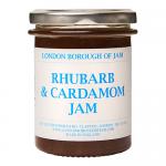 The photo shows six glass jars of Rhubarb & Cardamom jam arranged in a neat group. Each jar reveals a rosy-pink preserve dotted with tiny spice flecks. Uniform branded labels wrap the jars and metal lids catch soft light, creating gentle highlights on the glass.