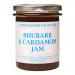 The photo shows six glass jars of Rhubarb & Cardamom jam arranged in a neat group. Each jar reveals a rosy-pink preserve dotted with tiny spice flecks. Uniform branded labels wrap the jars and metal lids catch soft light, creating gentle highlights on the glass.