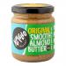 Six glass jars of Yumello Smooth Almond Butter sit in a neat row, each with a round white lid and a bright yellow label showing the brand name and almond illustration. The creamy light-brown spread is visible through the glass, and soft studio lighting highlights glossy surfaces. Soft glossy sheens.