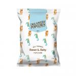 A glossy 100g bag labeled Dreamers Popcorn features a bold logo on a two-tone background of pastel pink and deep navy. Illustrated popcorn kernels and sugar crystals surround a clear window showing light golden sweet-and-salty popped kernels. Small text lists ingredients.