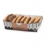 A rustic bakery pack sits open to reveal a neat stack of round, golden shortbread biscuits flecked with dark chocolate pieces. Crumbs scatter on a wooden board beside a linen cloth; the box shows a simple farmhouse label in muted tones, evoking a homely artisanal look. Soft golden edges, sugar glint