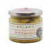Six clear glass jars sit in a neat group, each filled with chunky yellow-and-green piccalilli. Mustard-yellow labels with Dylan’s logo wrap the jars; glossy metal lids catch soft studio light. One jar is open, showing the briny, textured relish inside.