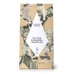 A glossy rectangular box of salted caramel truffles sits open, revealing fifteen round truffles nestled in a gold foil tray. Each chocolate displays a smooth dark shell with delicate sea-salt crystals, subtle surface sheen and gentle ridges, while warm caramel tones peek where cut or cracked. Shiny.
