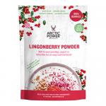 Six red-and-white sachets of Arctic Power Berries Lingonberry Powder sit on a light wooden table; one sachet is open, spilling fine, deep-red powder beside fresh lingonberries and green leaves under soft, natural light.