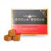 Photograph shows a neat rectangular box of eight round Booja-Booja truffles arranged in two rows. Each truffle is glossy dark chocolate with craggy honeycomb caramel centers revealed in one cut piece. Warm brown tones and subtle gold accents highlight artisanal detail. Linen liner adds subtle depth.
