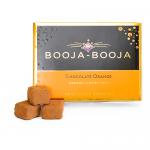 A compact box of eight glossy chocolate truffles nests in a clear tray beside a matte orange-and-brown sleeve. The sleeve shows orange slices and elegant script, while individual round truffles display glossy finishes and fine textured dusting under soft studio lighting. Soft highlights trace curves