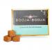 Compact rectangular pack displays eight round truffles arranged in two rows. Dark chocolate shells show glossy caramel swirls and a light sprinkle of sea salt. Warm brown and cream packaging bears the Booja-Booja logo against a neutral background. Soft glossy highlights and ultra faint cocoa dusting.