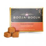 A small rectangular box sits against a white background, its matte brown sleeve featuring cream lettering. Eight round truffles peek from an open tray, each glossy dark chocolate studded with crushed hazelnut pieces and fine cocoa dust, hinting at a crunchy interior. Soft gloss catches faint sheens.