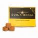 Close-up of a small rectangular box of Booja-Booja Almond Salted Caramel truffles. Matte brown and cream packaging shows elegant typography and an almond-splash graphic. Eight glossy, round truffles sit beside the box, their caramel centers hinting through slight cracks in the chocolate shells.
