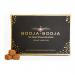 A compact rectangular box bearing the Booja-Booja logo sits centered on a neutral background. The cover shows elegant typography and subtle accents; five glossy chocolate pieces sit arranged in a neat row beside the opened box, each with smooth, rounded surfaces. Soft studio light creates depth and