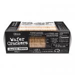 A close photo shows Olina's Bakehouse packaging beside several thin, pale-golden wafer crackers. The crackers lie stacked and scattered, their surfaces freckled with dark cracked-pepper bits. The branded box displays a bakery logo and product text against a neutral background Soft shadows add depth