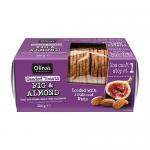 A rectangular pack of twelve 100g Olina's Bakehouse Seeded Toasts in Fig and Almond flavor sits upright. A clear window reveals thin golden-brown crisp toasts studded with sesame and flax seeds, visible fig pieces and slivered almonds; a simple label shows brand and flavor.