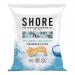 A matte seafoam-green packet sits against a pale background, its logo and minimalist waves printed in white. Crisp, irregular dark-green seaweed chips spill from the torn top, showing speckled salt crystals and a light, brittle texture that catches soft studio light. Subtle shadowing defines textures