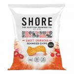 A neat stack of twenty-four compact 25g Shore Crisps pouches fills the frame; each glossy pouch displays the Shore Seaweed Chips logo and a bold red Sweet Sirarcha label. Dark green seaweed crisps peek through a clear window beside stylized ocean waves and chili illustrations soft salt-kissed sheen