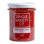 Six clear glass jars sit in a neat group, each topped with a metallic lid. Deep, glossy crimson jam fills the jars, flecked with chili seeds. Clean white labels display bold red and black lettering reading Single Variety Co Fireflame Chilli Jam, against a plain studio background. Subtle jar shadows.