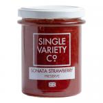 A row of six 220g Single Variety Co jars sits on a light surface. Transparent glass reveals bright red strawberry preserve with visible seeds and a glossy texture. Each jar has a simple white label and silver lid; soft natural light creates subtle reflections and shadows. A small paper tag hangs on.