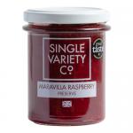 Six identical glass jars line up against a neutral background. Each jar shows glossy, deep ruby-red raspberry preserve with visible seeds. Cream-and-black labels read the variety name; gold metal lids reflect soft studio lighting.