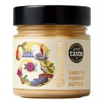 A clear jar of Butternut of London Smooth Peanut Butter sits on a neutral surface. The jar shows a creamy, glossy tan spread with a smooth top. A clean label wraps the jar with the brand name and simple graphics; a screw lid finishes the package. Soft studio lighting creates a gentle highlight. Tone.