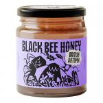 Six glass jars of Black Bee British Autumn Honey sit in a neat row, amber honey catching warm light. Each 227g jar has a black lid and a cream label featuring a stylized black bee and autumnal accents. The jars rest on a wooden surface against a soft neutral background. Soft daylight adds depth too.