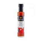 Six 250ml clear bottles of bright red Sriracha stand in a neat cluster. Each bottle shows a white label reading The Coconut Kitchen with a small coconut icon and white cap. The vivid sauce contrasts with the crisp, tropical-style label.