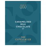 A smooth caramelised milk chocolate bar rests in a crinkled foil-lined wrapper, its surface glossy with faint molded ridges and a broken corner revealing soft caramel strands. Warm brown tones, subtle sheen and scattered crumbs emphasize creamy texture and rich filling. Soft reflections catch light.