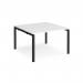 The photograph shows a pair of sleek black framed bench desks, with a clean white tabletop. The desks are designed to be placed back to back, measuring 1200mm x 1200mm. This modern and functional set-up is perfect for any contemporary office space.