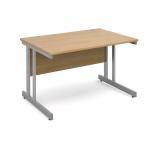 This picture shows a sleek Dams International Desking Momento straight desk with a silver cantilever frame and an oak top. The desk measures 1200mm by 800mm and is perfect for any modern office setting. Its clean lines and neutral colors make it a versatile choice for any workspace. The desk exudes a professional and minimalist look, providing ample space for work and organization. The sturdy silver cantilever frame adds a touch of elegance to the desk, while the oak top adds warmth and sophistication. This desk is both functional and stylish, making it a great addition to any office space.