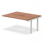 The photo features a modern and stylish dynamic bench desk from the Evolve Plus collection. The desk has a beautiful walnut top with a clean white frame, creating a sleek and professional look. This versatile desk is perfect for any modern office space.
