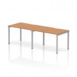 This picture showcases a sleek, modern office setup with two people working at a Dynamic Bench Desking Evolve Plus 1200mm Single Row. The desk features an elegant oak top and a sturdy silver frame, creating a stylish and functional workspace.