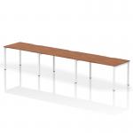 The photograph features a sleek and modern work space with a single row of three person office bench desks. The desks have a rich walnut top and are supported by a clean, white frame. The overall design exudes functionality and style, perfect for a dynamic work environment.