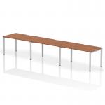 This photograph captures a sleek and modern office setup featuring a 1400mm single row Evolve Plus bench desk in walnut with a silver frame. The dynamic design allows for 3 people to comfortably work together, promoting collaboration and productivity.