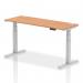 The picture shows a spacious office desk measuring 1600 x 600mm with a sleek oak top and silver adjustable legs. The desk also features cable ports for a tidy work space. Its dynamic design allows for both sitting and standing positions, promoting a healthier and more ergonomic workspace.
