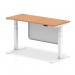 This image shows a sleek and modern office desk with a width of 1400mm and a depth of 600mm. The desk features an oak top and white steel legs with a white steel modesty panel. It also has built-in cable ports for easy organization. The desk is height adjustable, allowing you to use it in a seated or standing position.