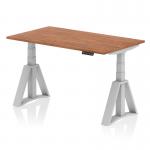 The picture shows a sleek and modern height adjustable desk in a beautiful walnut finish with a silver leg and piste foot design. The desk has a spacious 1400 x 800mm surface, perfect for a dynamic sit-stand workspace. Its adjustable feature allows for customizable height to accommodate different preferences and needs. Ideal for any office setup.