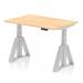 This photograph shows a sleek and modern office desk with a dynamic sit-stand feature. The desk has a maple top and silver legs, with adjustable height options. The unique Piste Foot adds a stylish touch to this functional desk.