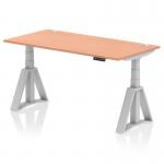 The image shows a sleek and modern height adjustable office desk with a beech top and silver legs. The desk features cable ports and a Piste Foot for added stability. Its dimensions are 1600 x 800mm and it can easily switch between sit and stand positions for a dynamic work experience.